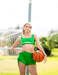 Woman in green athletic wear holding a basketball on a sports court