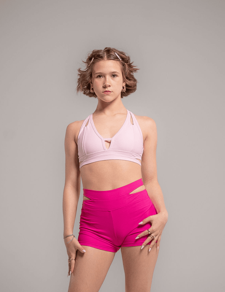 Woman wearing a pink sports bra and shorts on a gray background