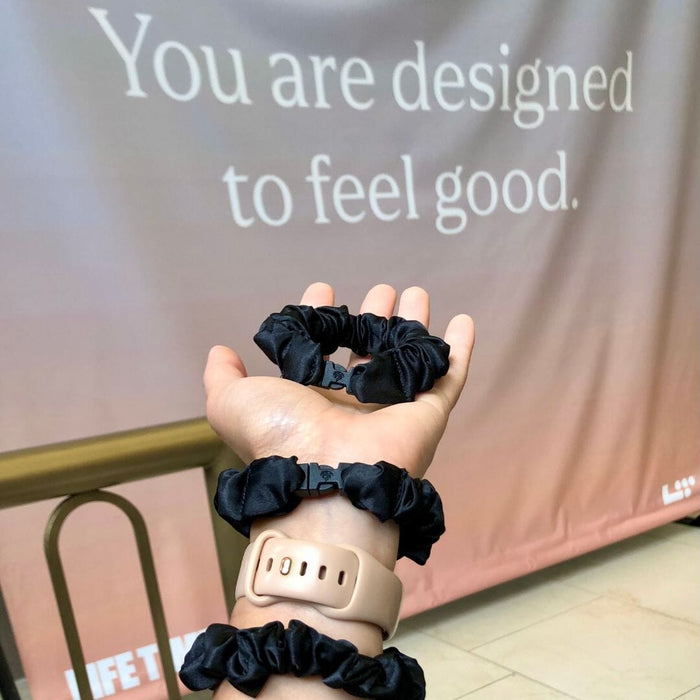 Hand holding three black scrunchies with a motivational quote in the background