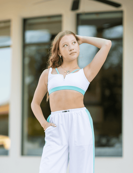 Woman wearing a white and turquoise sports bra and leggings in front of a blurred background