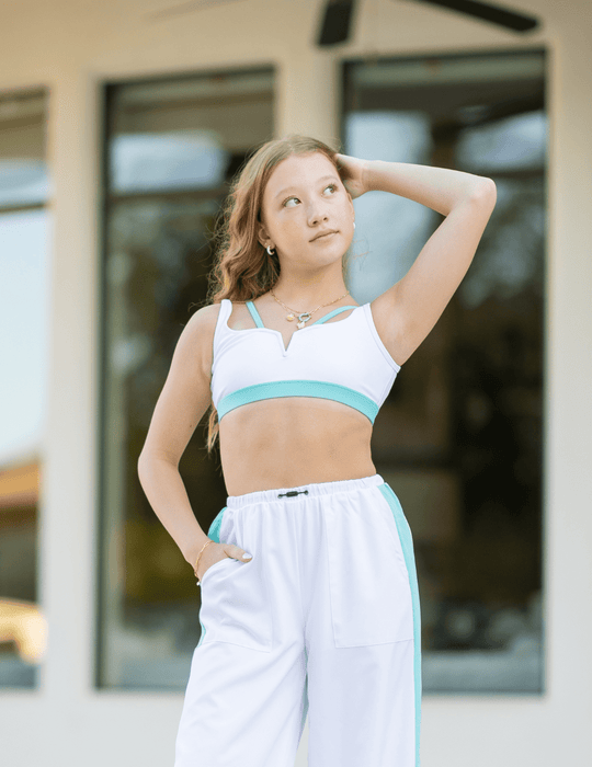Woman wearing a white and turquoise sports bra and leggings in front of a blurred background