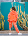 Person wearing an orange tracksuit standing in front of a teal wall with cacti.