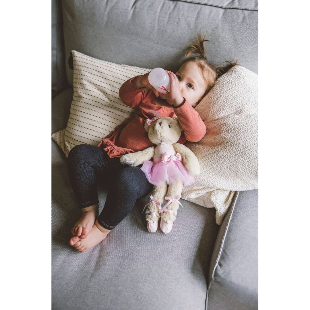 Child sitting on a couch with a teddy bear wearing a pink outfit