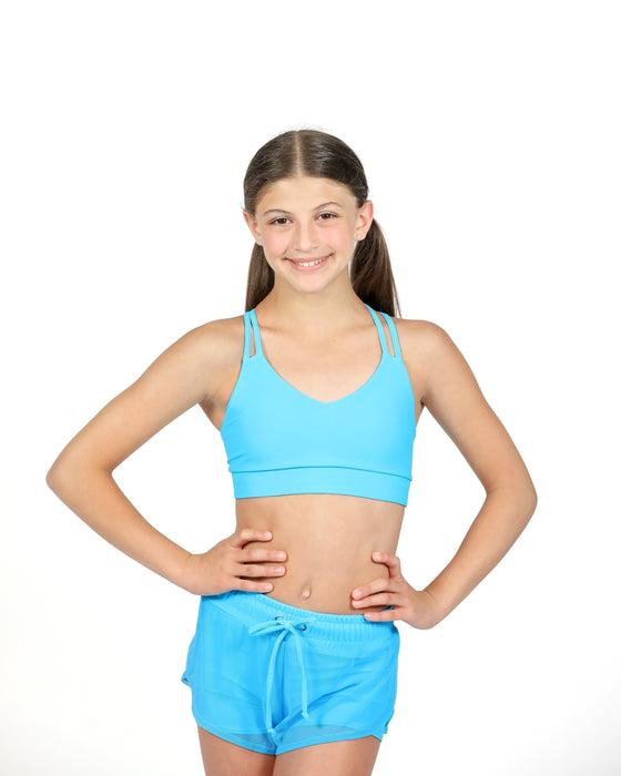 Young girl wearing a blue sports bra and shorts on a white background