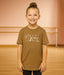 Young girl wearing a brown t-shirt with a graphic design in a dance studio.