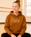 Person wearing a brown hoodie with a graphic design and text, sitting indoors.