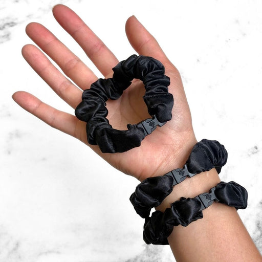 Hand holding three black scrunchies with a white marble background