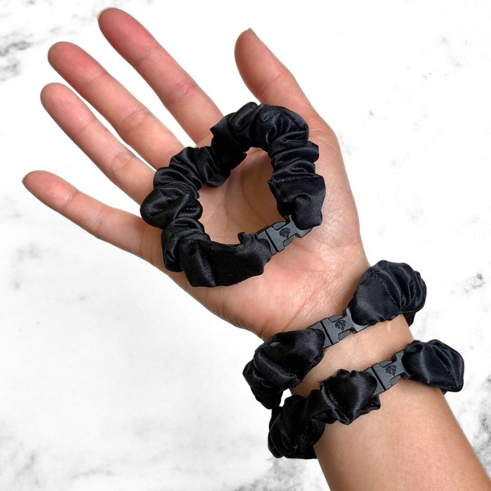 Hand holding three black scrunchies with a white marble background