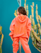 Person wearing a bright orange hoodie and pants with 'CHLAC' branding, standing in front of cacti.