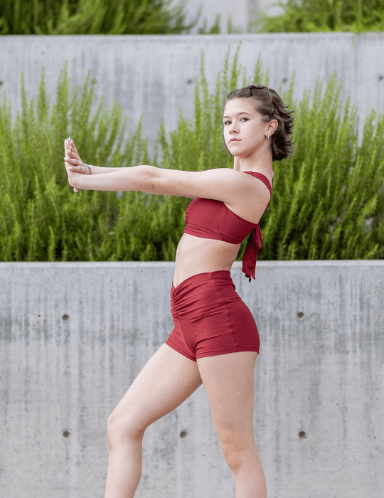 Woman in a red outfit standing outdoors with greenery in the background