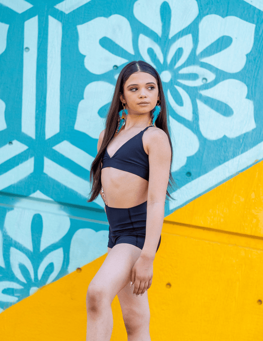 Woman in black athletic wear standing against a colorful wall with geometric patterns.