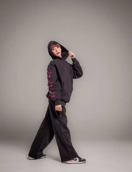 Person wearing a black hoodie with pink star designs on sleeves against a gray background