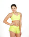 Woman wearing a bright yellow sports bra and shorts on a white background