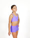 Young girl wearing a purple sports bra and shorts set on a white background