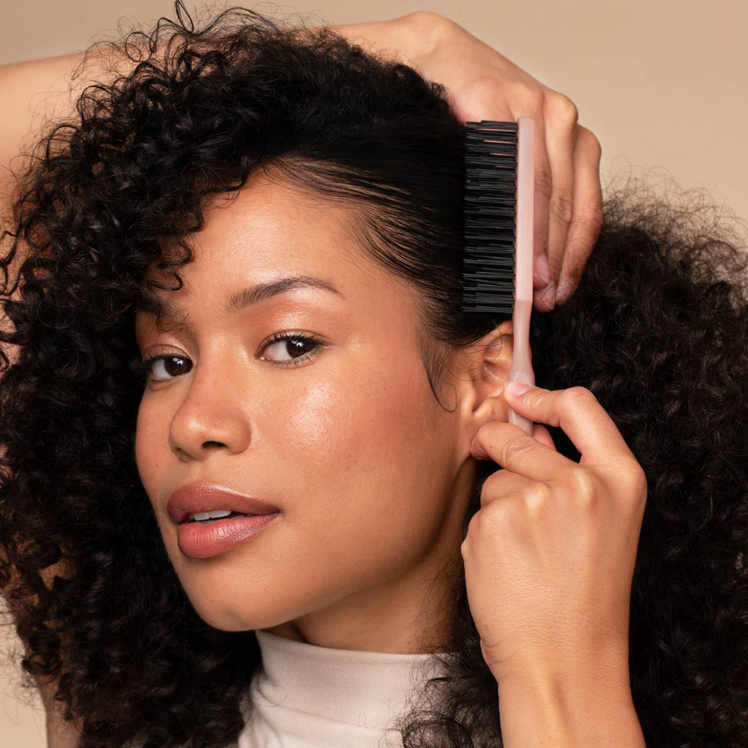 Woman with curly hair being styled with a comb against a beige background