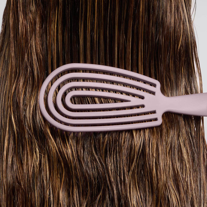 Pink hairbrush being used on brown hair against a neutral background