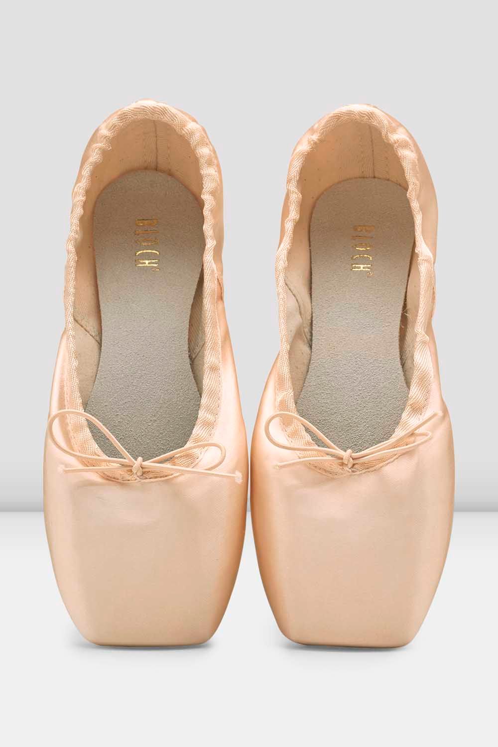 A pair of light peach satin ballet pointe shoes with square toes and ribbon bows, shown from a top-down view on a light gray background.
