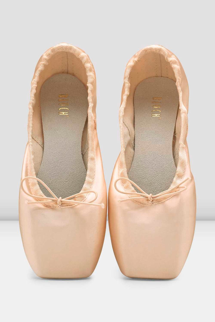A pair of light peach satin ballet pointe shoes with square toes and ribbon bows, shown from a top-down view on a light gray background.