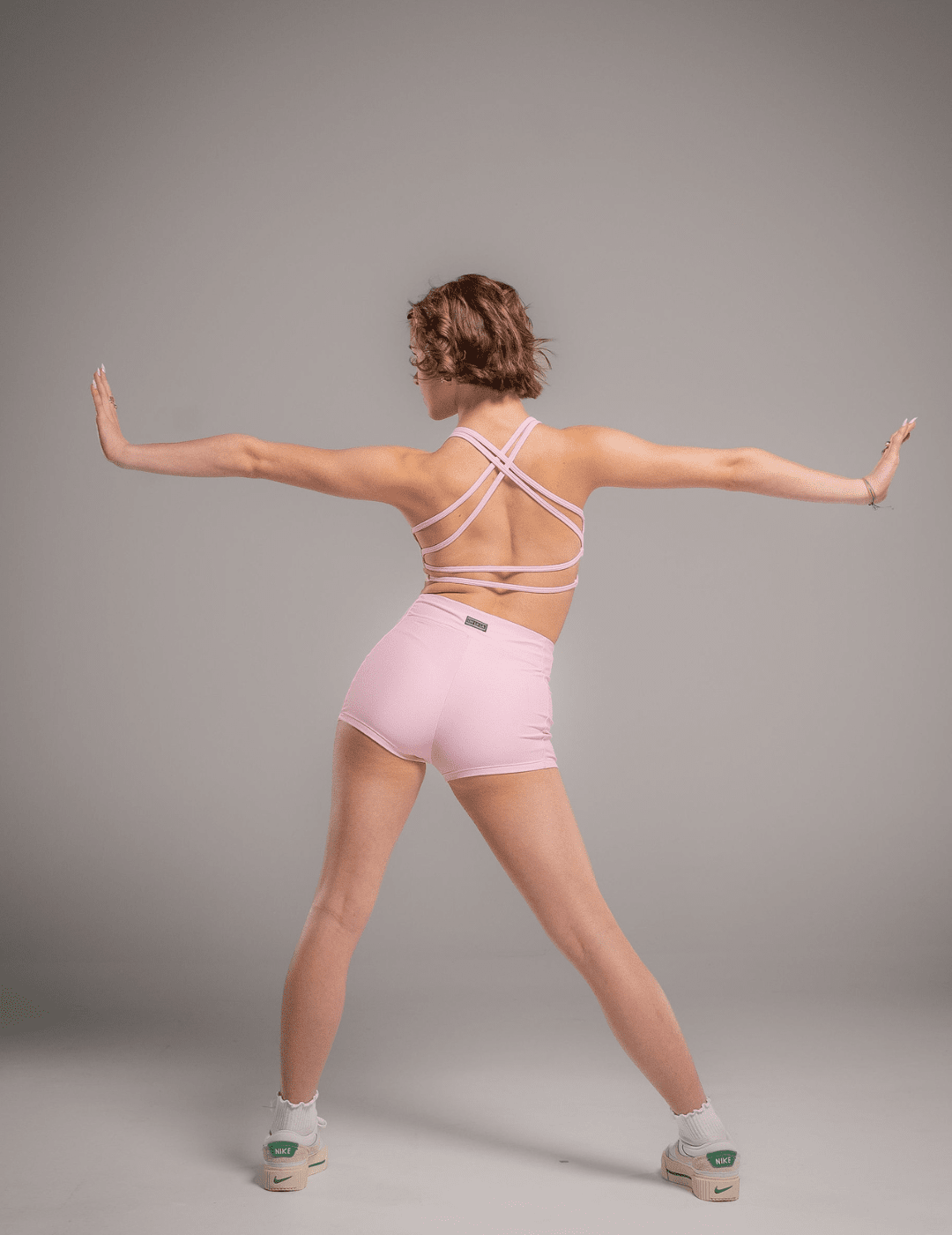 Person wearing a pink sports bra and shorts set on a gray background