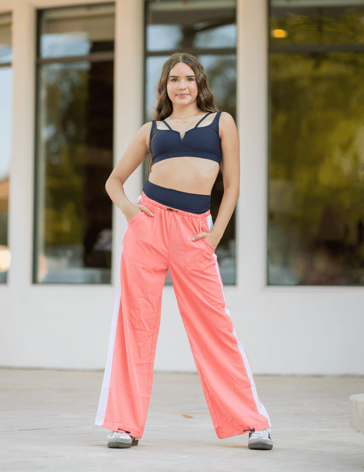Woman wearing a navy sports bra and pink pants standing outdoors.