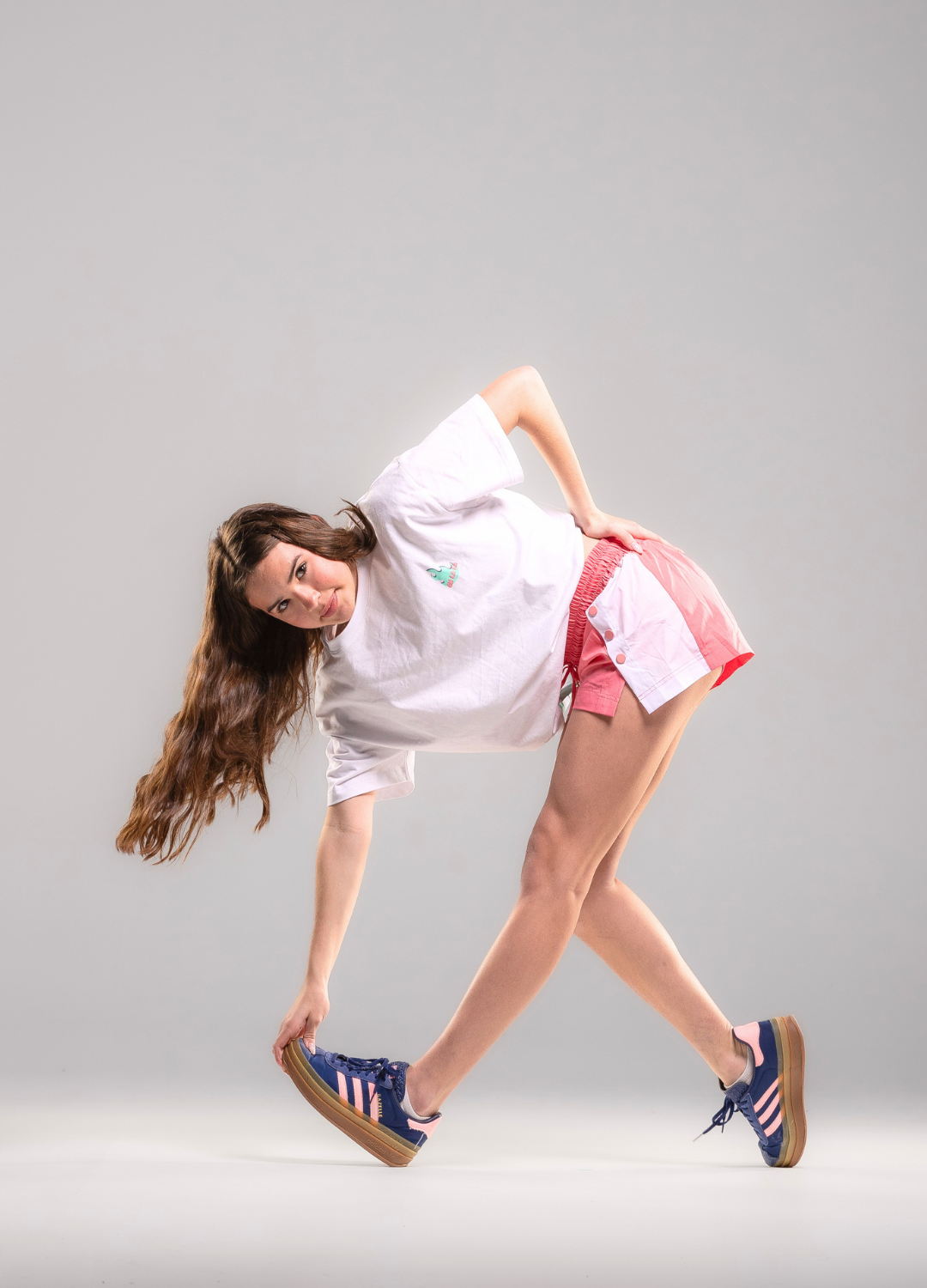 Woman posing in a white t-shirt and pink shorts on a gray background