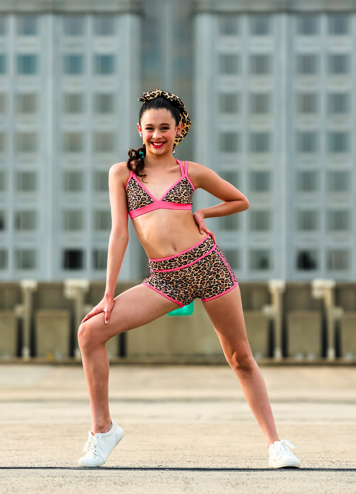 Woman in leopard print sports bra and shorts posing outdoors with a building in the background