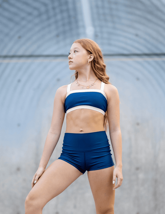 Woman wearing a blue sports bra and shorts against a gray background