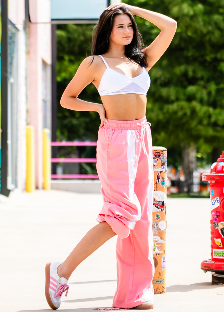 Woman in white sports bra and pink pants walking outdoors.