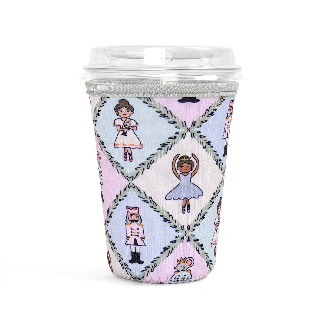 A reusable coffee cup with a clear lid and a pastel diamond-patterned sleeve featuring ballerina and nutcracker illustrations, shown on a white background.