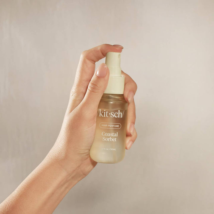 Hand holding a 'kit-sch' perfume bottle against a neutral background