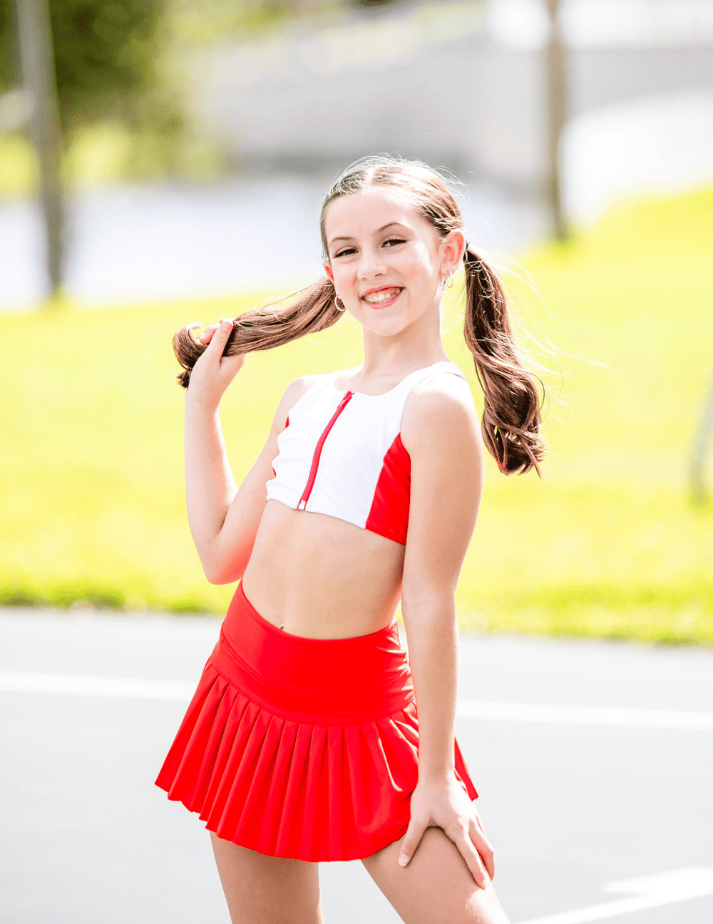 Young girl in a red and white outfit standing outdoors with a blurred background