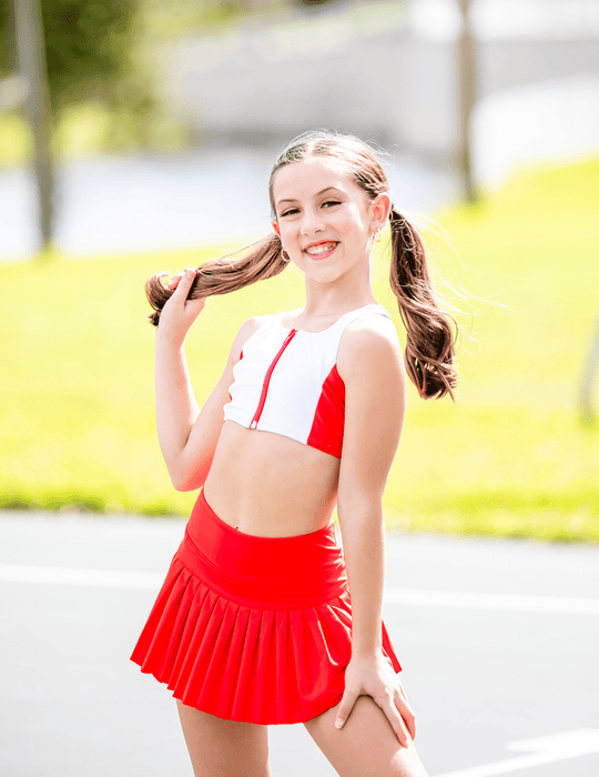 Young girl in a red and white outfit standing outdoors with a blurred background