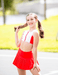 Young girl in a red and white outfit standing outdoors with a blurred background
