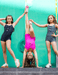 Three young girls in swimsuits posing against a teal wall.