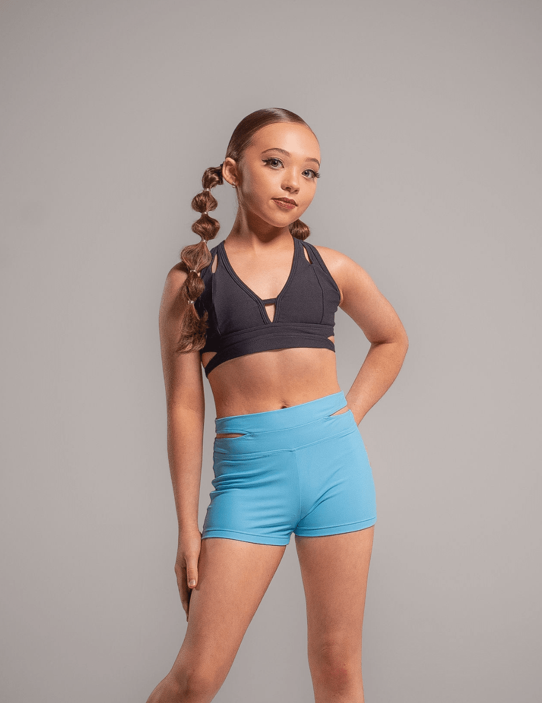 Young girl wearing a black sports bra and blue shorts against a gray background