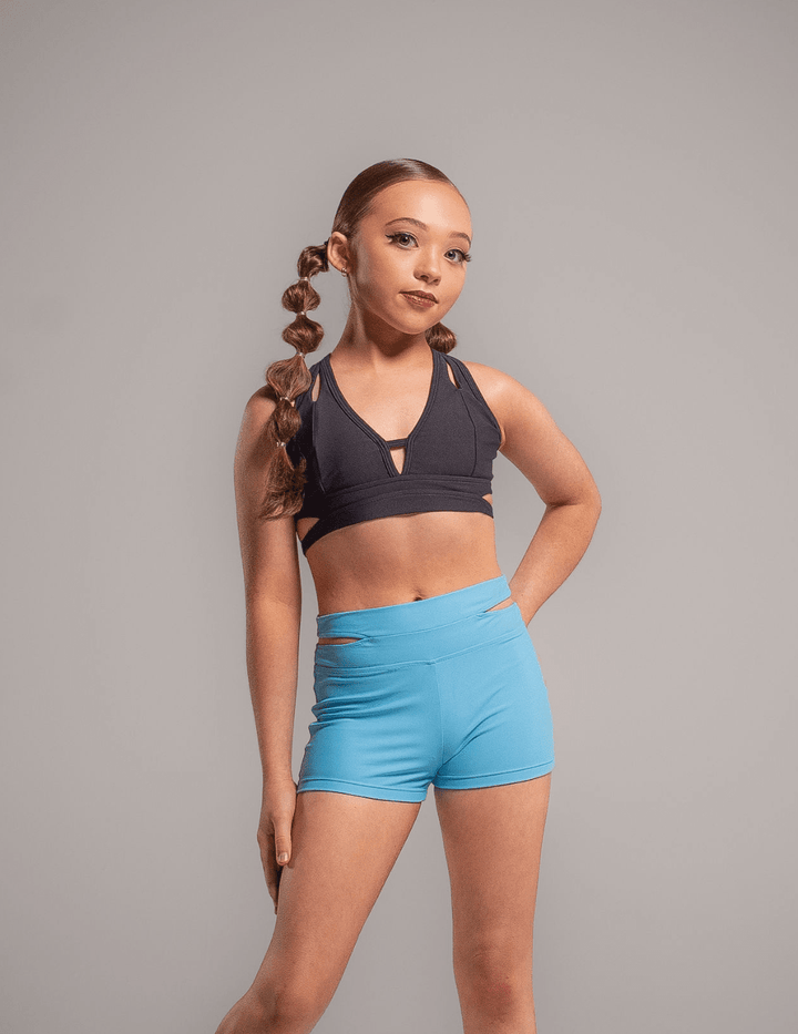 Young girl wearing a black sports bra and blue shorts against a gray background