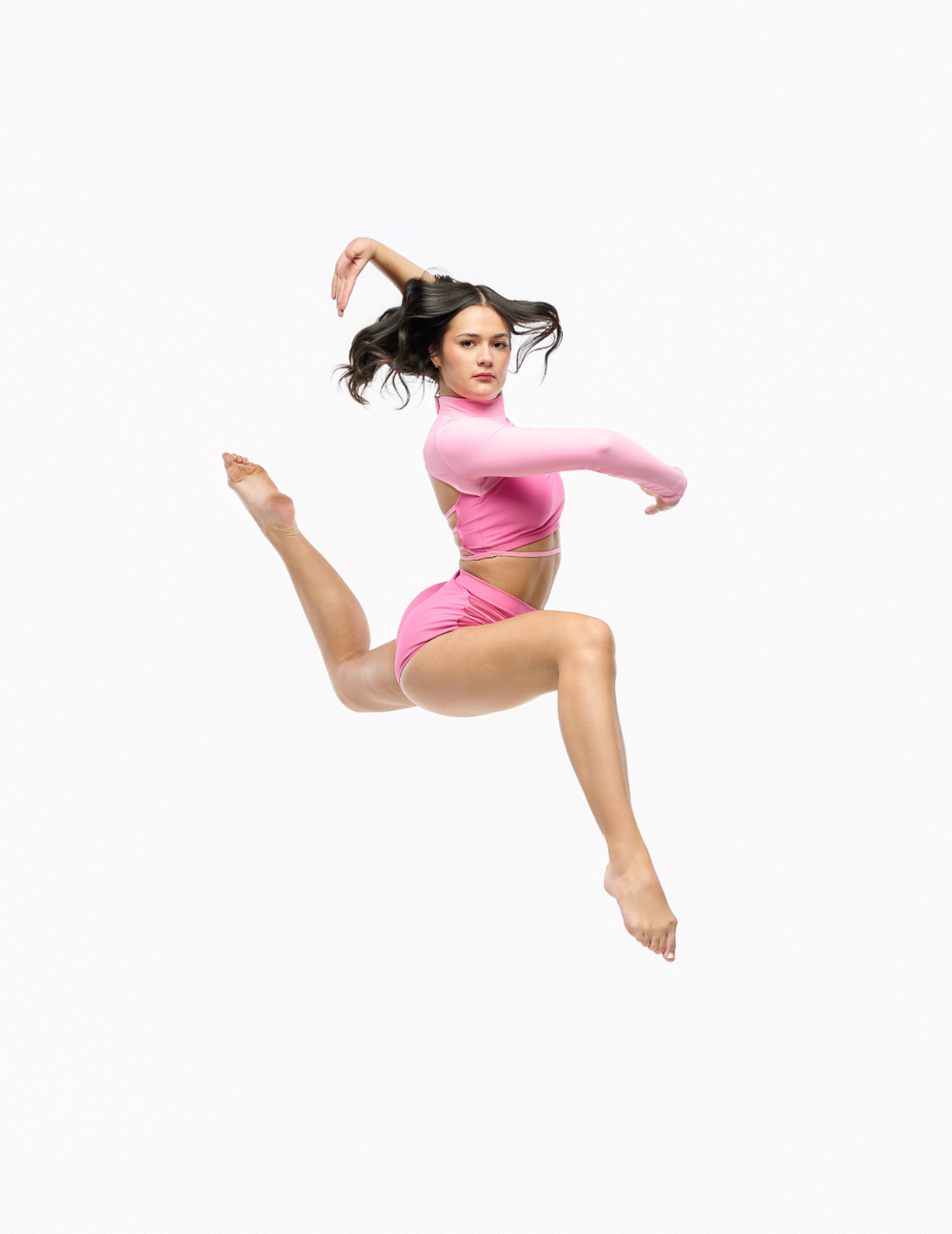 A woman in a pink dance or gymnastics outfit jumps against a solid white background, showcasing her dynamic pose with one leg extended and arms in motion.