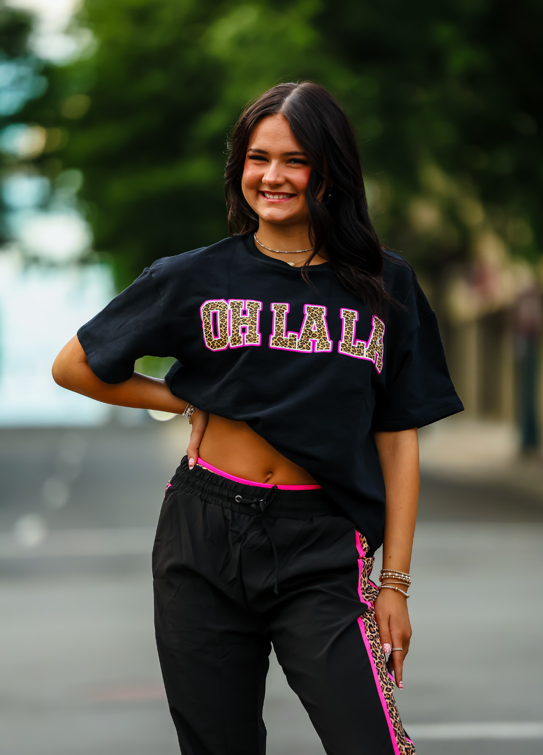 Woman wearing a black oversized t-shirt with 'OH LA LA' text, standing outdoors.