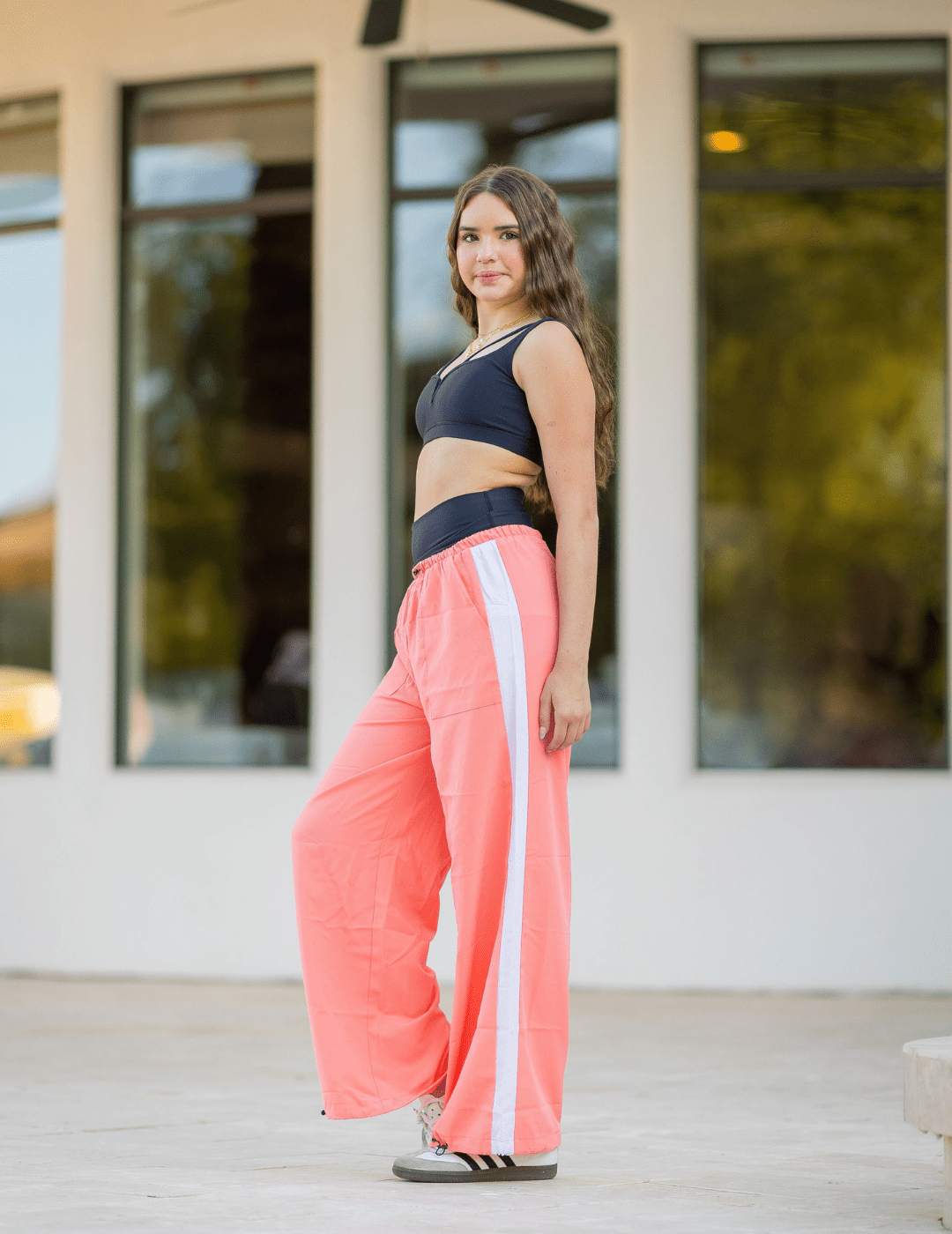 Woman wearing a black sports bra and pink pants with a white stripe outdoors.