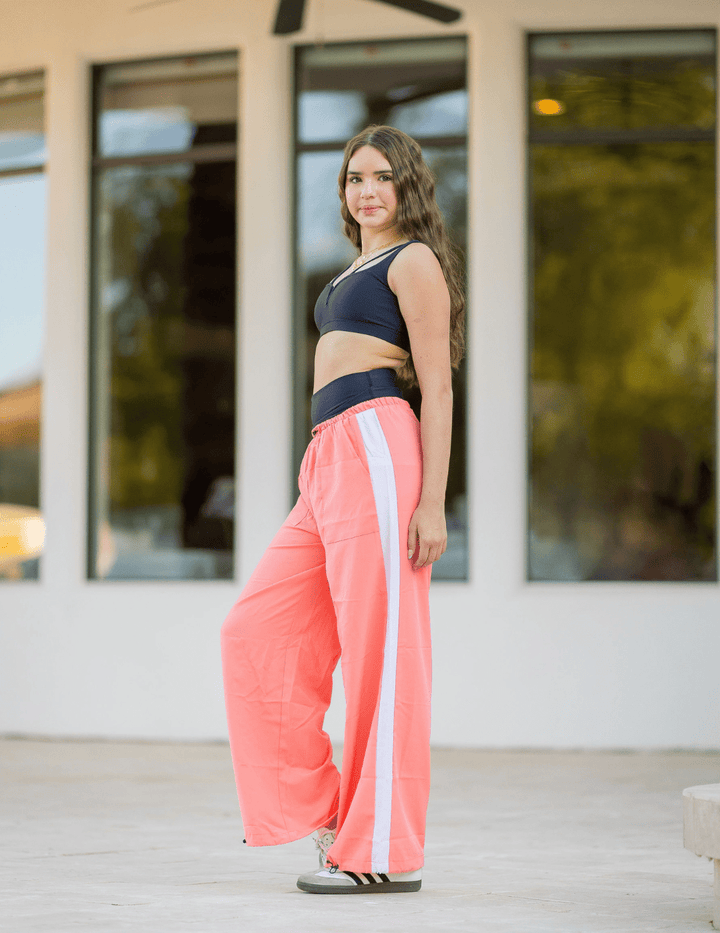 Woman wearing a black sports bra and pink pants with a white stripe outdoors.