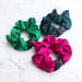 Three satin scrunchies in green, pink, and black on a white marble background