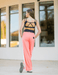 Woman wearing a black sports bra and pink pants standing in front of a building with large windows.