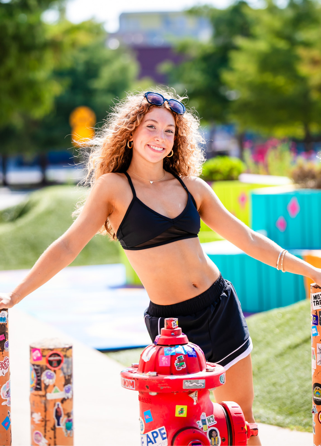 Woman posing next to a red fire hydrant with colorful stickers in an outdoor setting