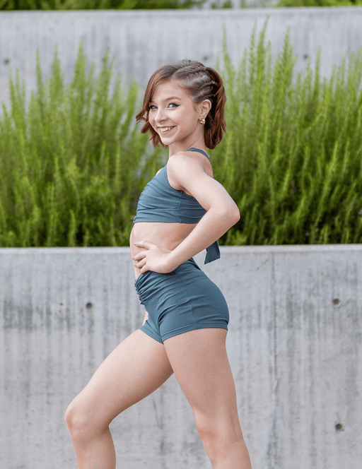 Woman in a blue athletic outfit standing outdoors with greenery in the background