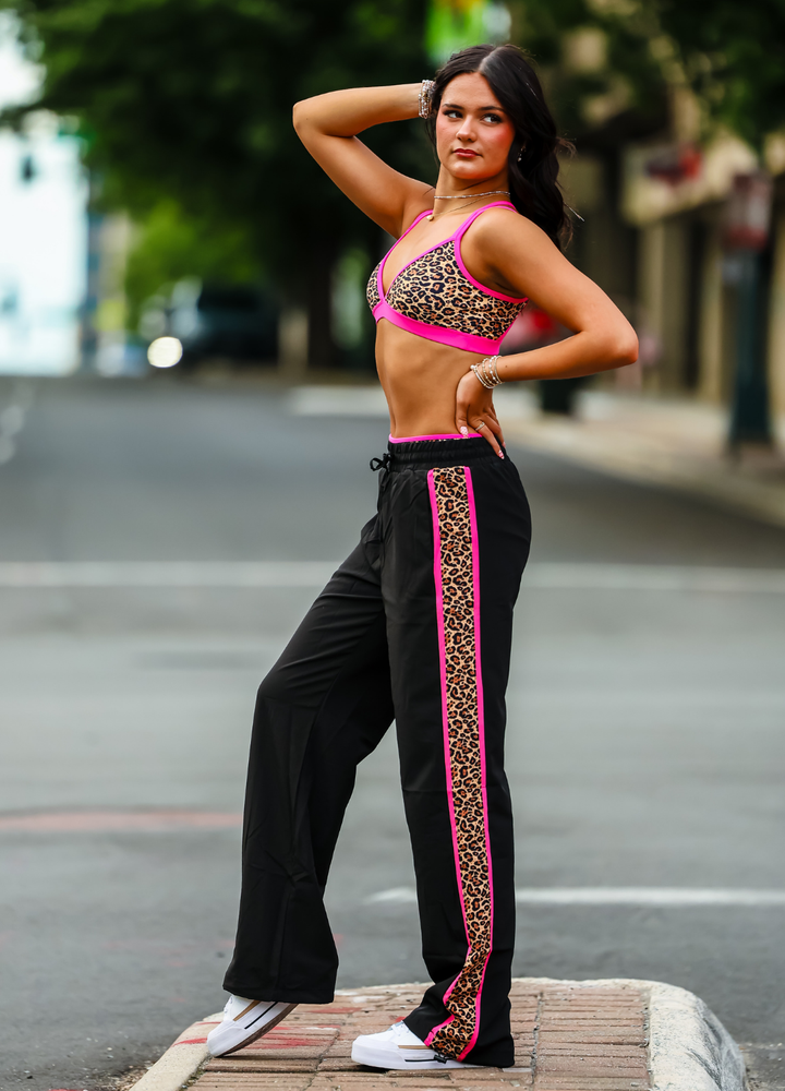 Woman in a leopard print sports bra and black pants with pink trim on a city street.