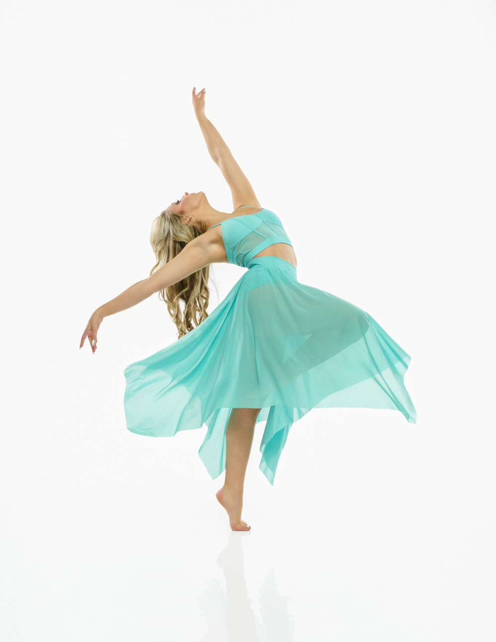 A woman in a flowing mint green two-piece dance outfit poses dynamically against a seamless white background.