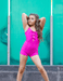Woman in a bright pink swimsuit posing against a teal wall.