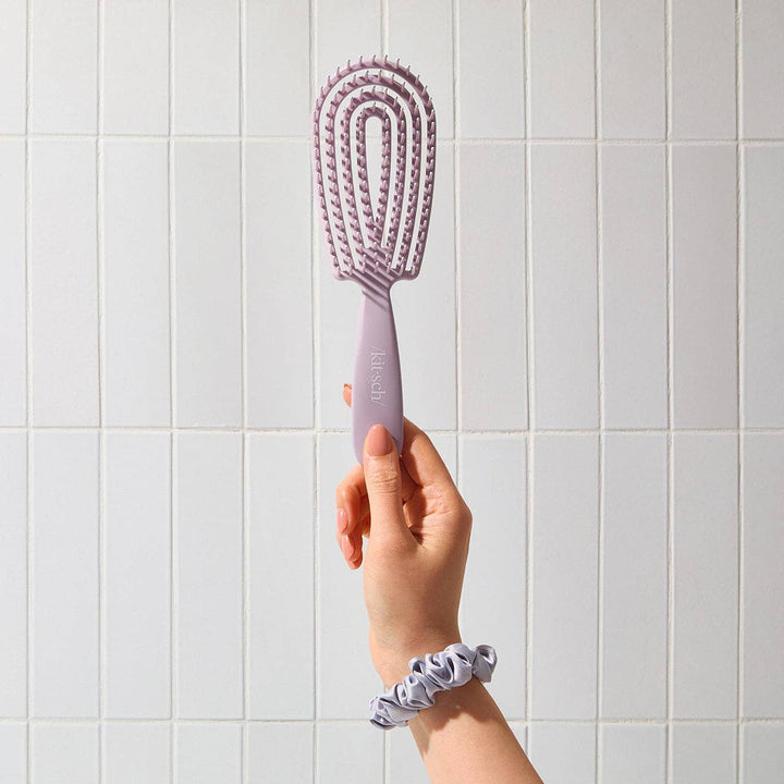 Hand holding a purple hairbrush against a tiled wall background