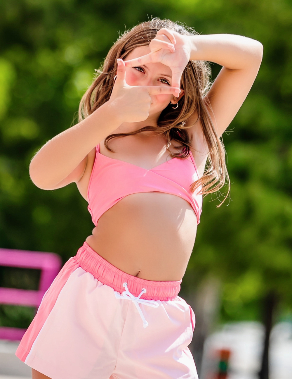 Young girl in pink outfit making a peace sign outdoors