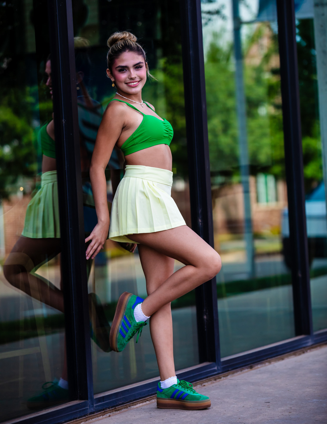 Woman in green top and yellow skirt posing in front of a glass door.